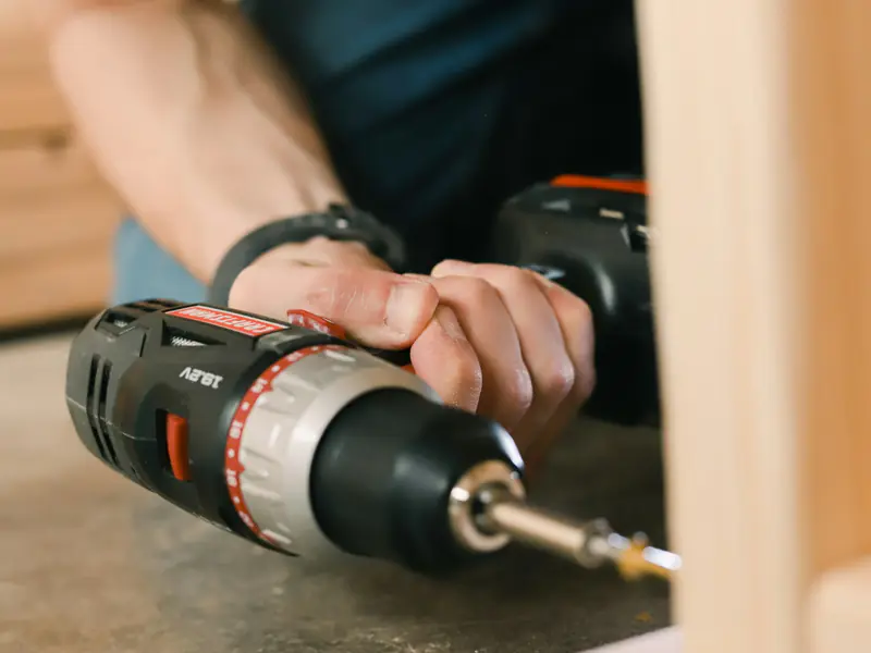 Hands driving a screw into a wooden frame with a cordless drill
