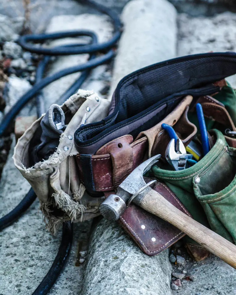 A worn leather tool belt with a hammer and pliers resting on a job site